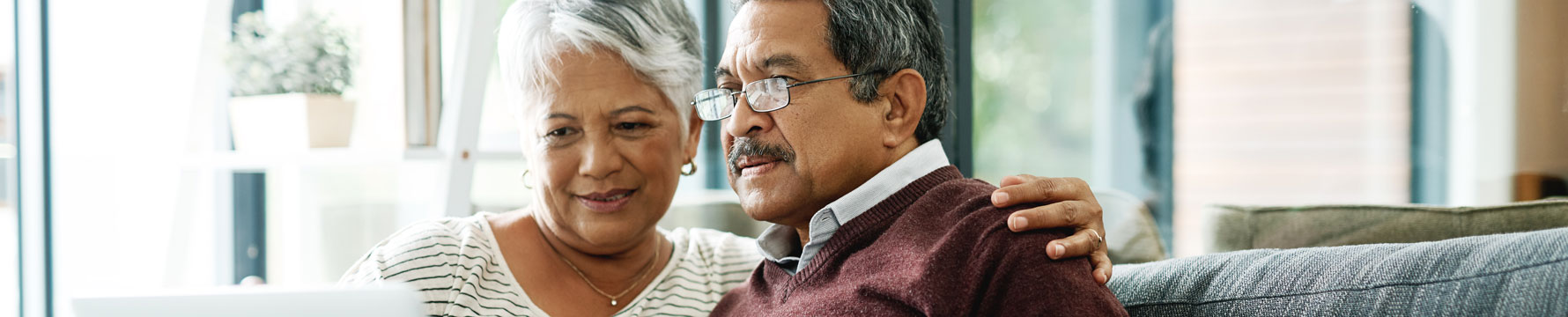 An elderly couple sitting on a couch looking at a laptop