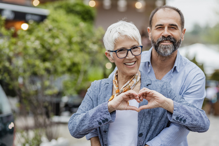 Cheerful mature couple looking at the camera and woman is making heart shape symbol with her hands.